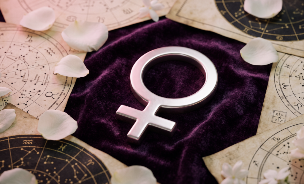 Símbolo astronômico de Vênus sobre veludo roxo com pétalas e mapas estelares, representando as previsões do horóscopo de hoje.