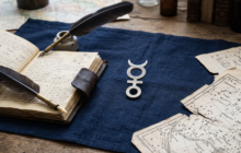 Símbolo astrológico de Mercúrio sobre linho azul com caderno antigo e pena, representando a regência da quarta-feira no horóscopo de hoje.
